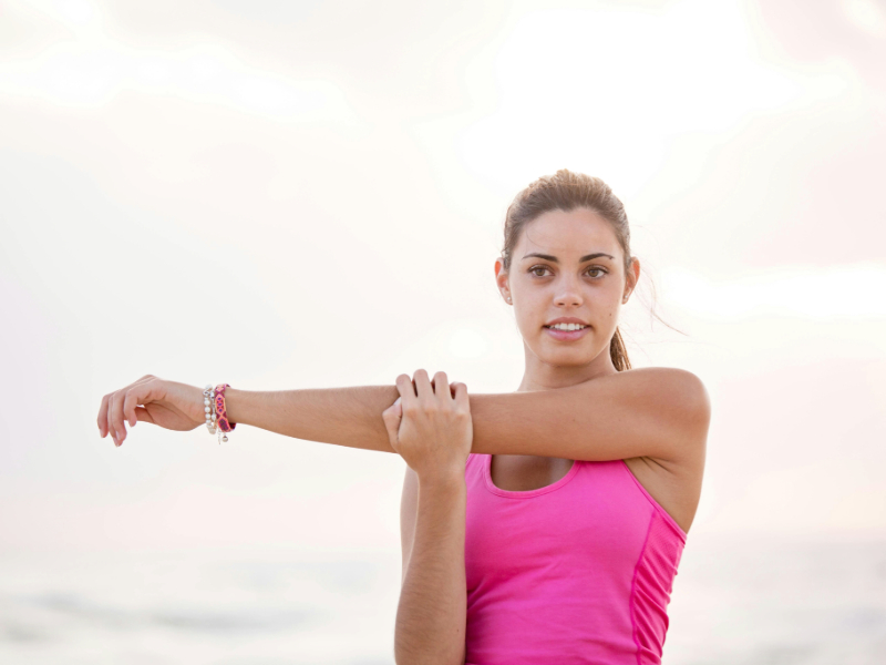 Beginner doing shoulder stretch in a bright outdoor space